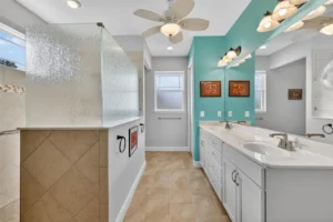 Modern bathroom featuring a dual sink vanity, glass shower, and light blue accent wall complemented by neutral tiles.