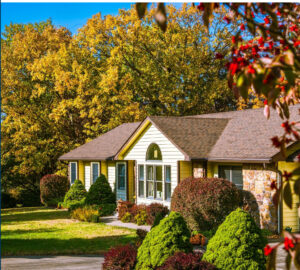 A cozy yellow house surrounded by vibrant autumn foliage and neatly trimmed bushes, illuminating a peaceful suburban atmosphere.