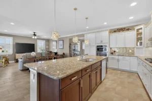 A modern kitchen featuring a large island with granite countertop, white cabinets, pendant lighting, and an open layout connecting to a dining area.