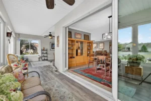 A cozy room with a sitting area, showcasing wooden furniture, large windows, and a glimpse of an outdoor space.
