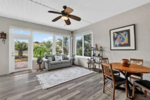 A bright, cozy living area with a sofa, dining table, and large windows showcasing greenery outside.