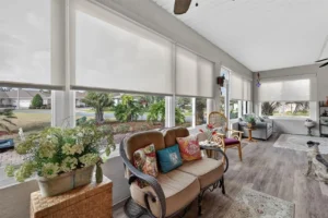 A cozy sunroom with a comfortable couch, decorative pillows, houseplants, and large windows allowing natural light.