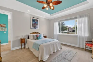 Brightly decorated bedroom featuring a large bed, wooden accents, and a ceiling fan, with natural light streaming through a window.
