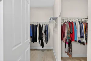 A well-organized closet with hanging clothes in various colors, showcasing a neat arrangement and light wood flooring.