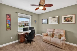 A cozy home office with a computer desk, comfortable chair, couch, and wall art in a softly colored room.