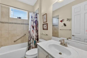A bright bathroom with a shower, bathtub, and decorative artwork, featuring neutral tones and natural light from a window.