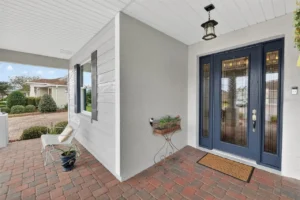 A stylish entryway featuring blue double doors, paver flooring, and decorative elements like a hanging lamp and planters.