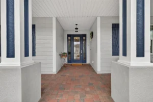 An inviting entryway showcasing a blue door, brick flooring, and white columns with a minimalistic design.