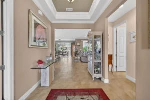 A spacious foyer with a decorative carpet, elegant decor, and a view into a well-lit living area beyond.
