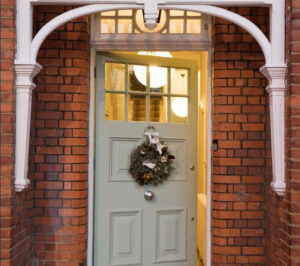 A charming mint green door adorned with a festive wreath, framed by elegant architectural details and brickwork.